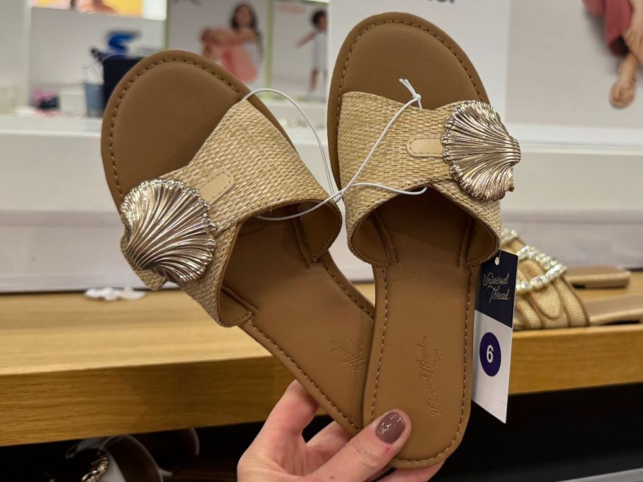 Hand holding a pair of Universal Thread Women's Nesryn Raffia Shell Ornament Slide Sandals 