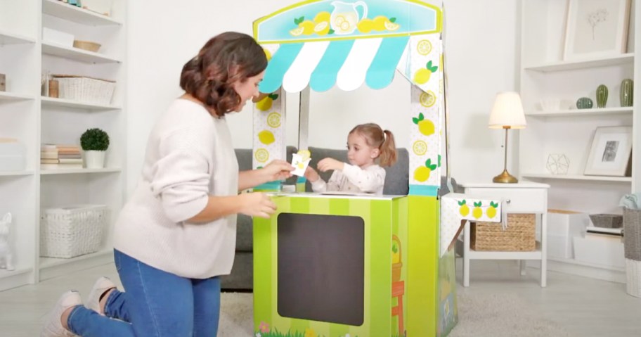 mom kneeling at lemonade stand with daughter serving her a cup