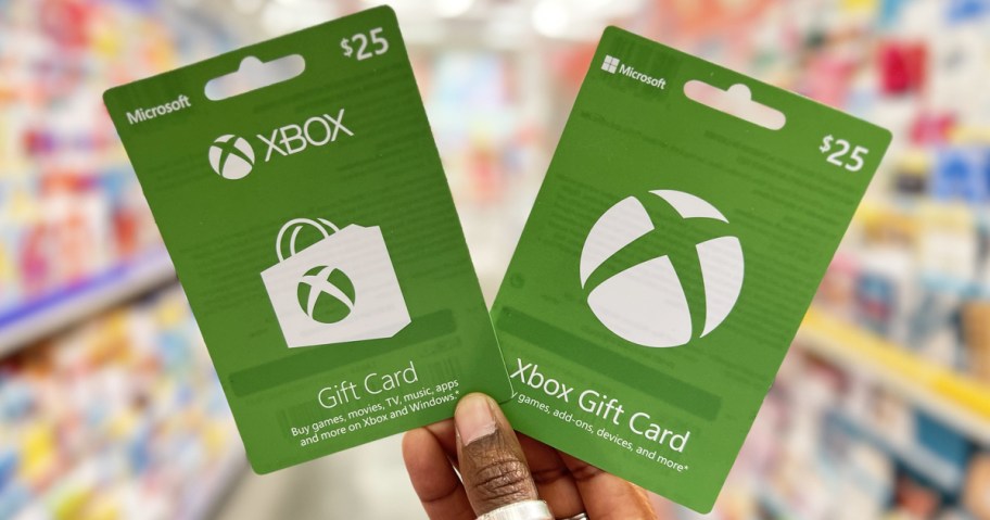 hand holding up two green Xbox gift cards in store