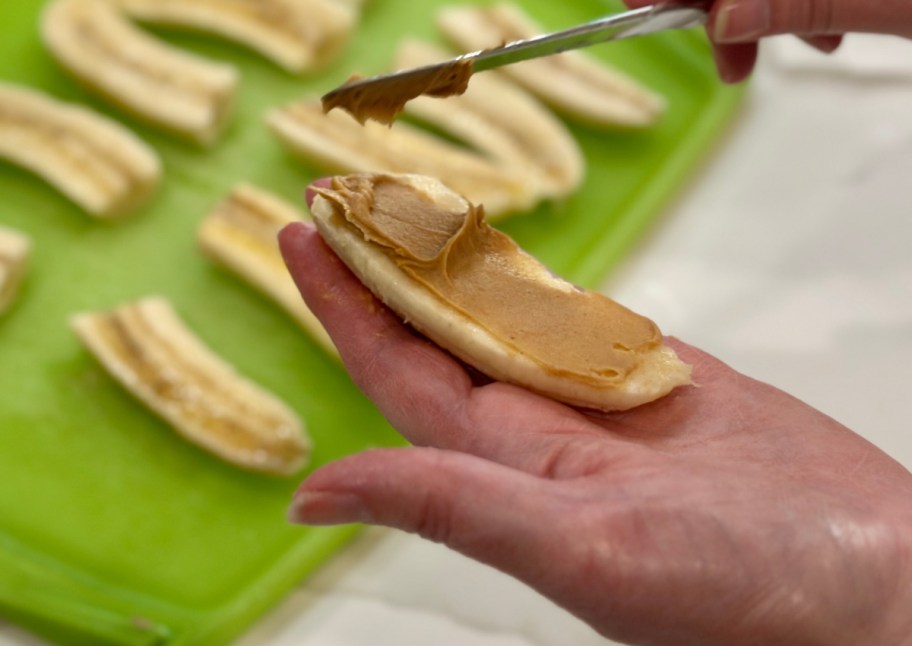 hand holding banana spreading peanut butter on it