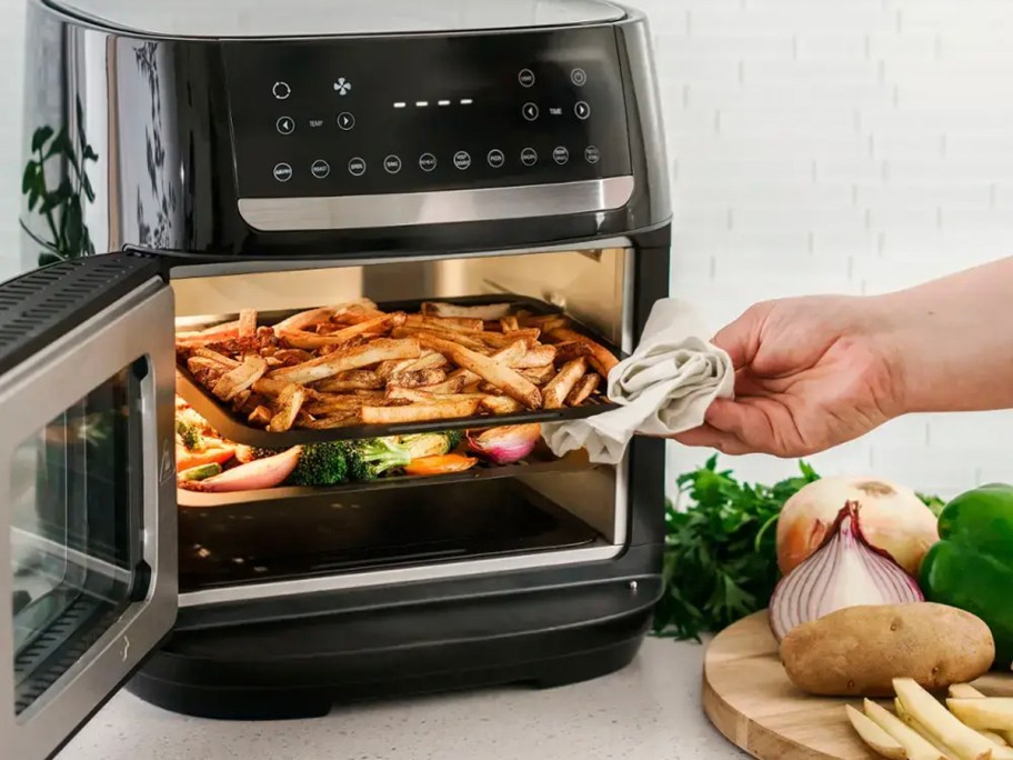 hand taking tray of fries out of black and silver air fryer 