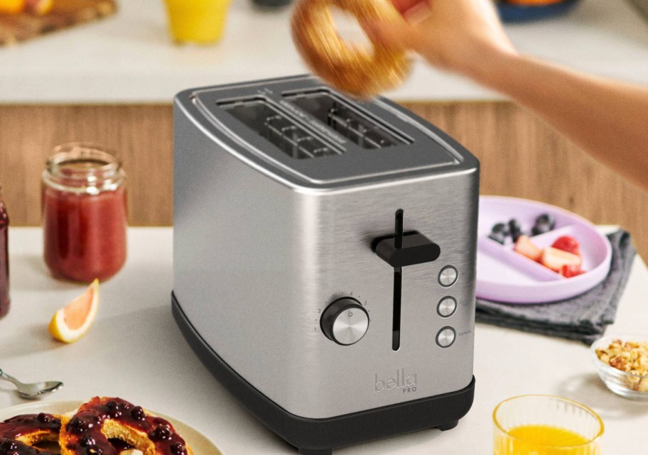 hand holding bagel on top of stainless steel toaster