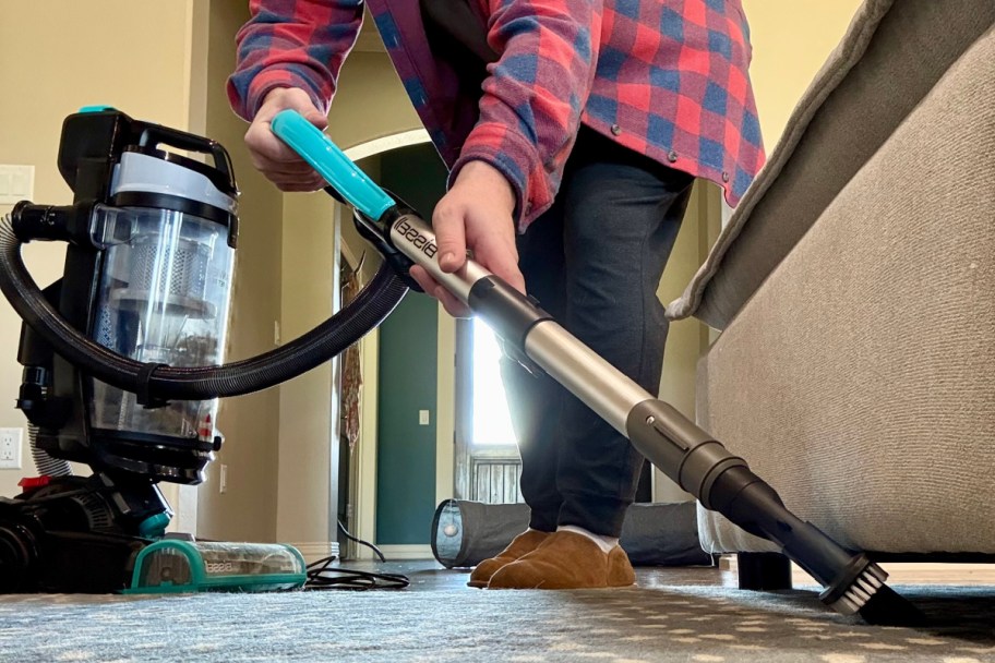 man using vacuum wand to clean under couch