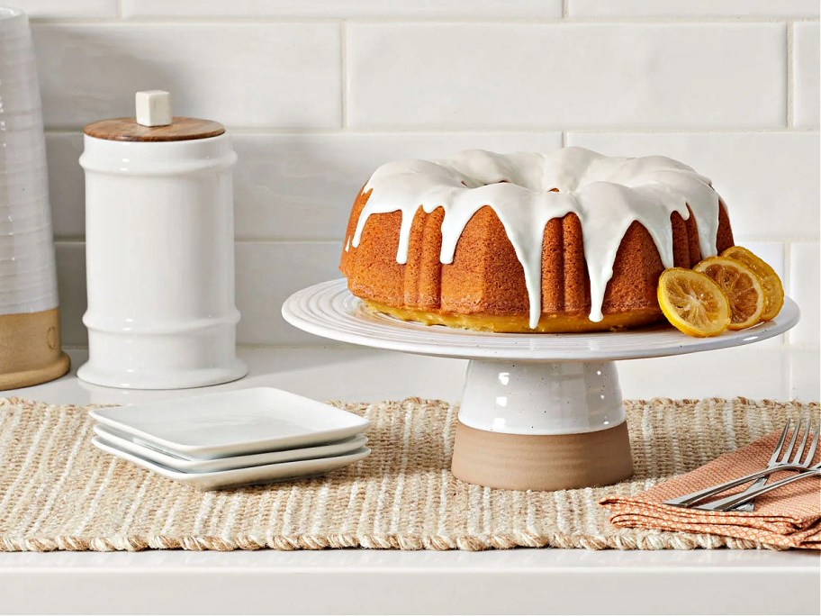 cake stand with a bundt cake on top sitting on a counter near plates and a canister