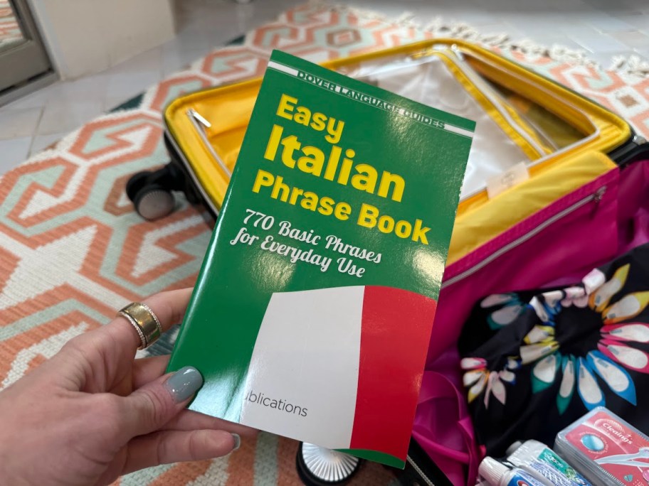 hand holding easy italian phrase book over suitcase