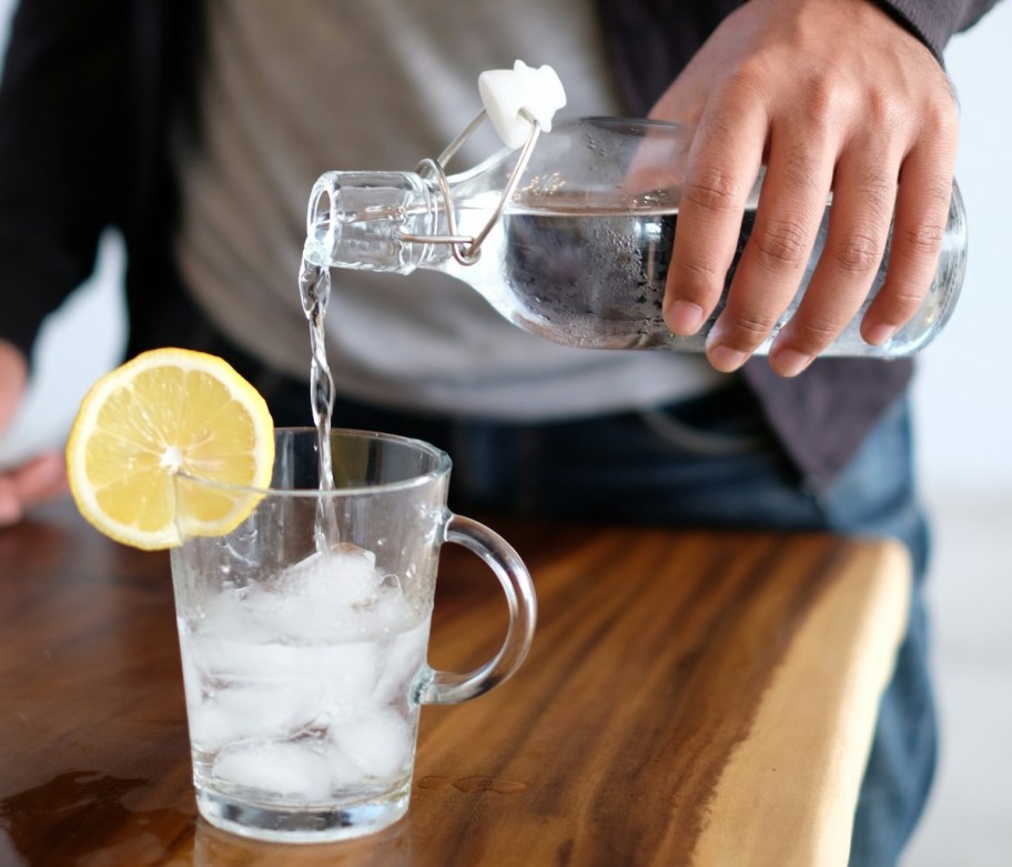 hand pouring water in clear glass with lemon