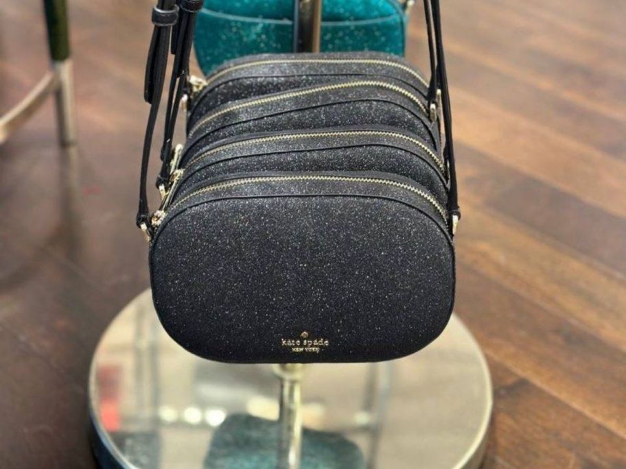 black Kate Spade New York Glimmer Oval Camera Bags hanging in store