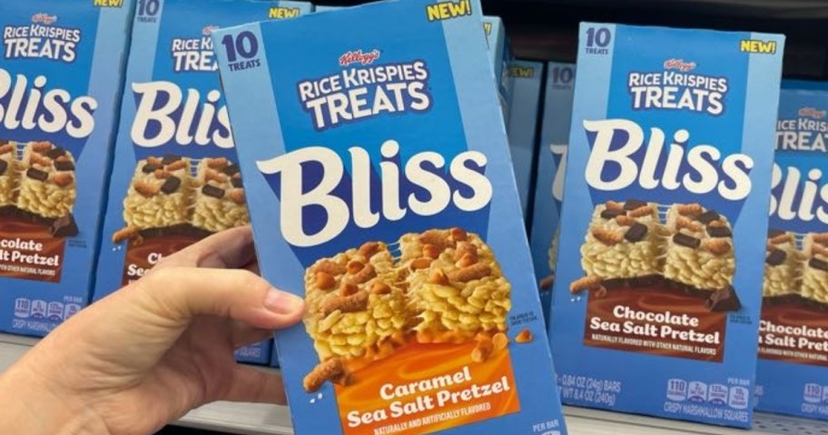 hand holding a box of Rice Krispie Treats Bliss bars, more on a store shelf behind it