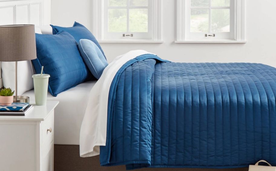 a bed with a blue satin quilt and matching shams