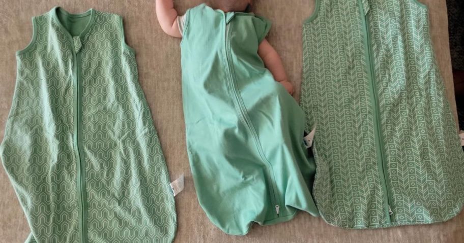 baby wearing sleep sack on blanket next to two other green sleep sacks