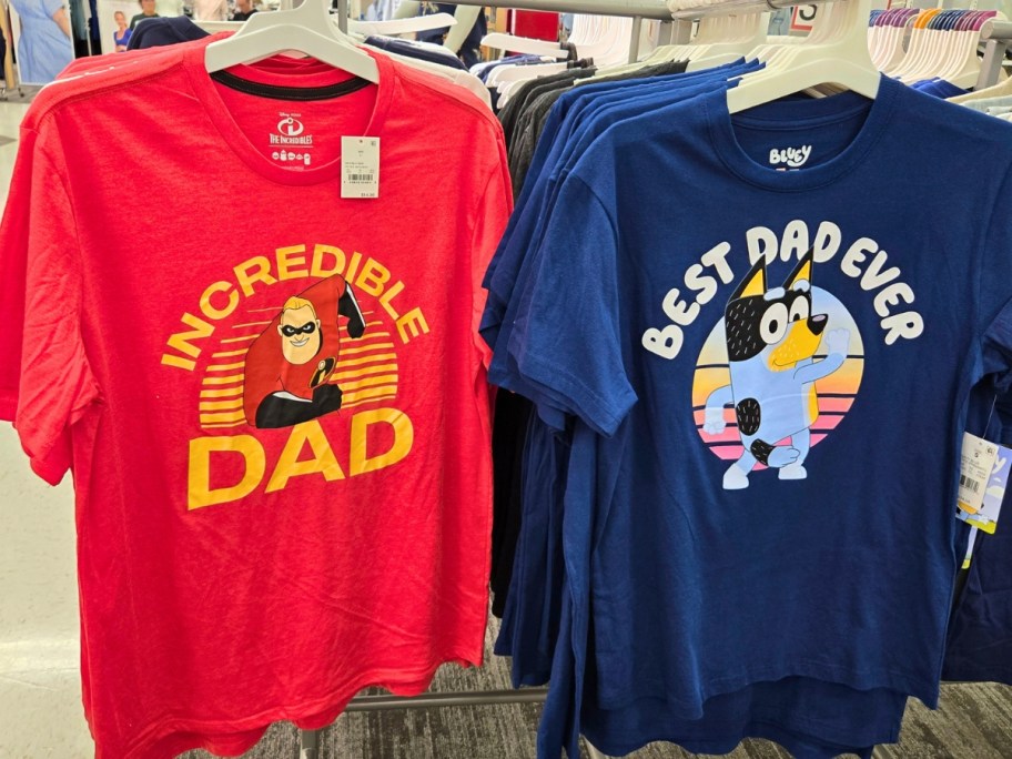 2 Dad t-shirts hanging on a store rack, one is red with Mr. Incredible and says "Incredible Dad" and the other is blue with Bluey and says "Best Dad Ever"