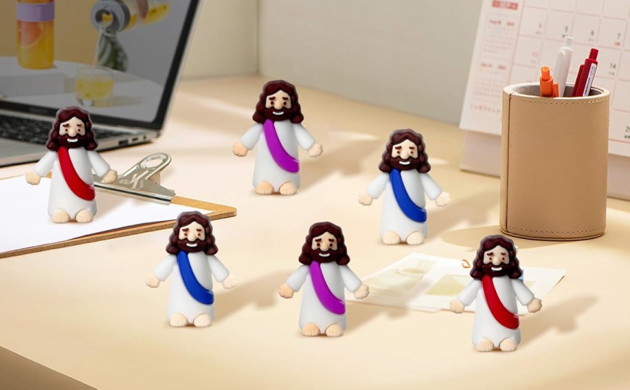 small plastic jesus figurines displayed on a desk near a laptop