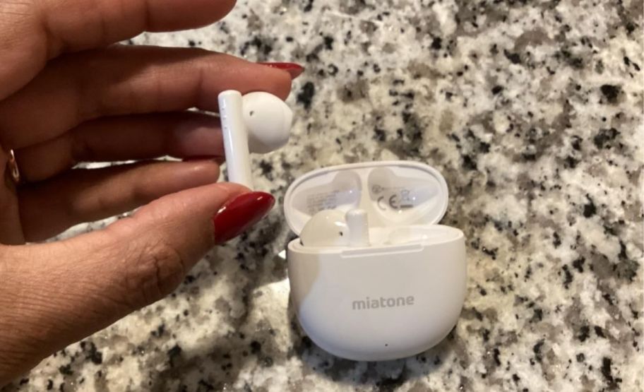 a womans hand holding a wireless earbud next to a charging case