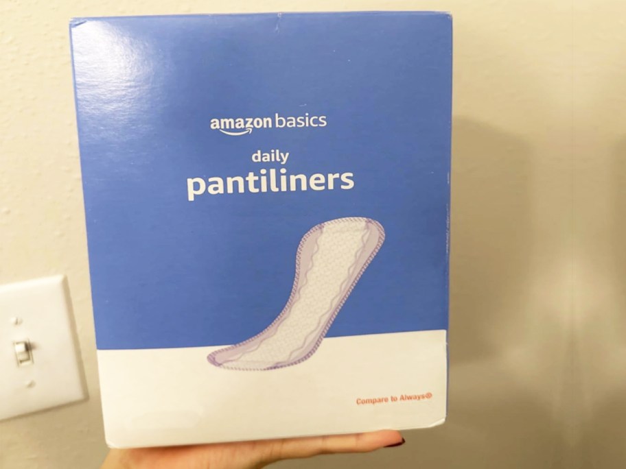 hand holding up a blue and white box of Amazon Basics Daily Pantiliners