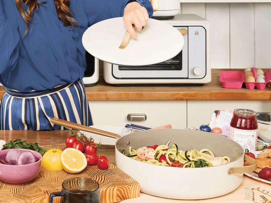 Woman lifting the lid off of a Beautiful by drew barrymore sautee pan