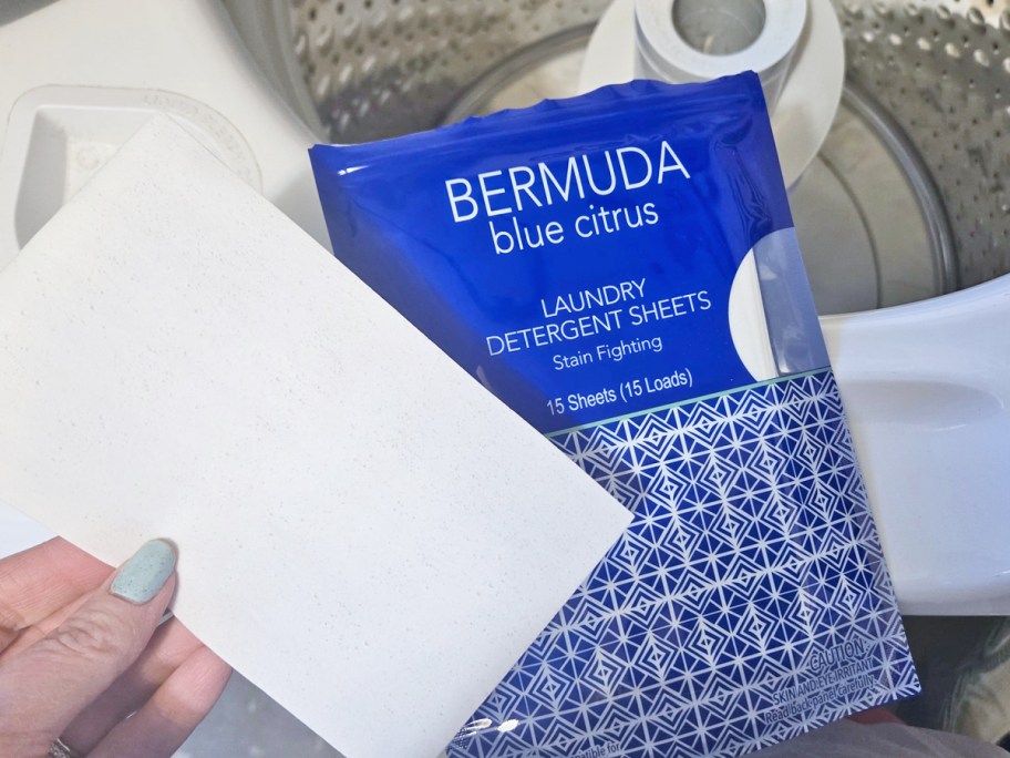 hand holding a laundry detergent sheet next to opened washing machine