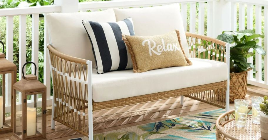 A wicker loveseat with pillows on it 