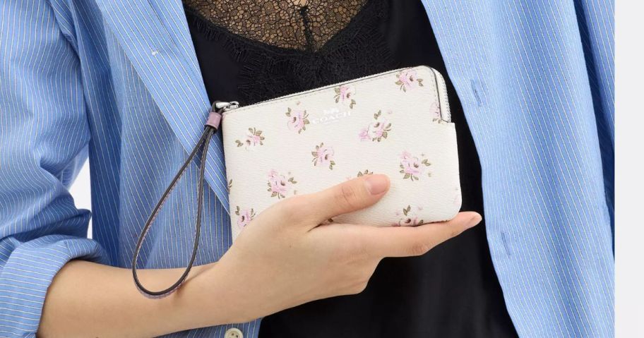 A woman holding a Coach wristlet in floral print