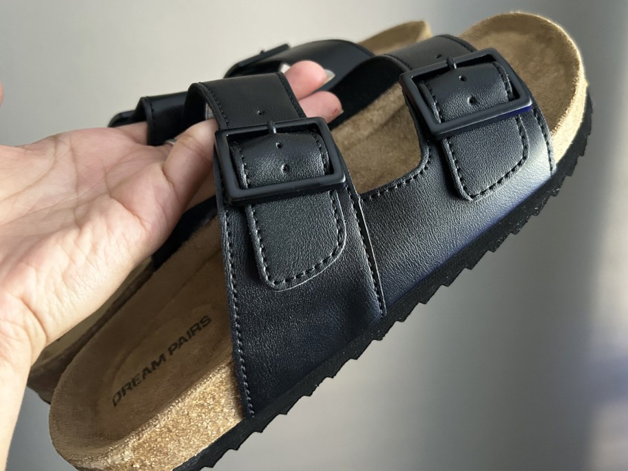 hand holding up a pair of black double buckle footbed sandals