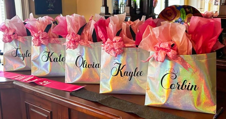 15 iridescent gift bags with pink tissue paper sitting on a table