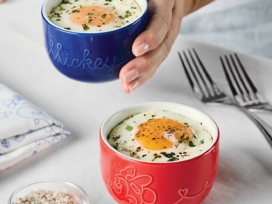 Hand holding disney ramikens with an egg inside of it