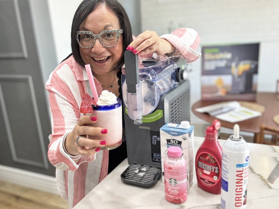 woman standing next to a slushie machine and holding up a frozen pink drink