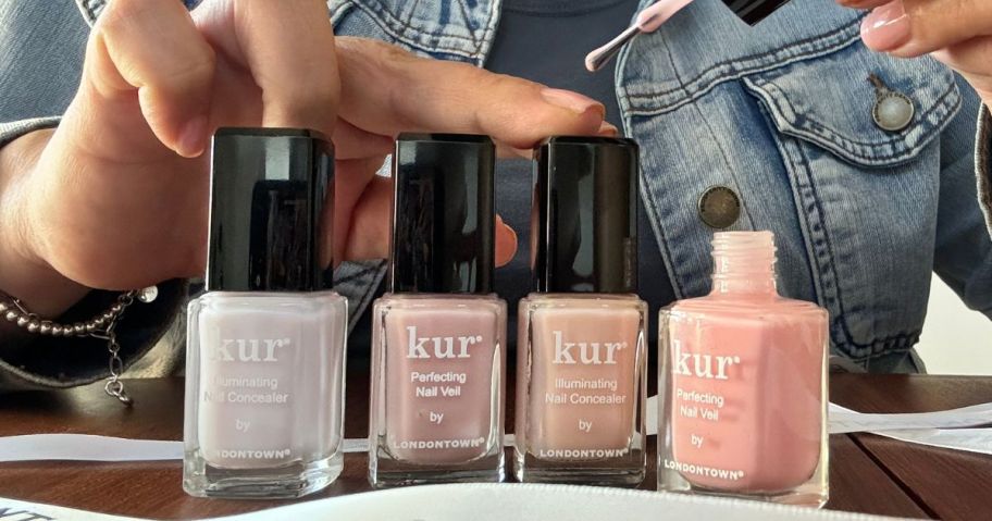 4 Bottles of Londontown Nail Polish with one open and a woman using the brush to apply it to her fingernail 