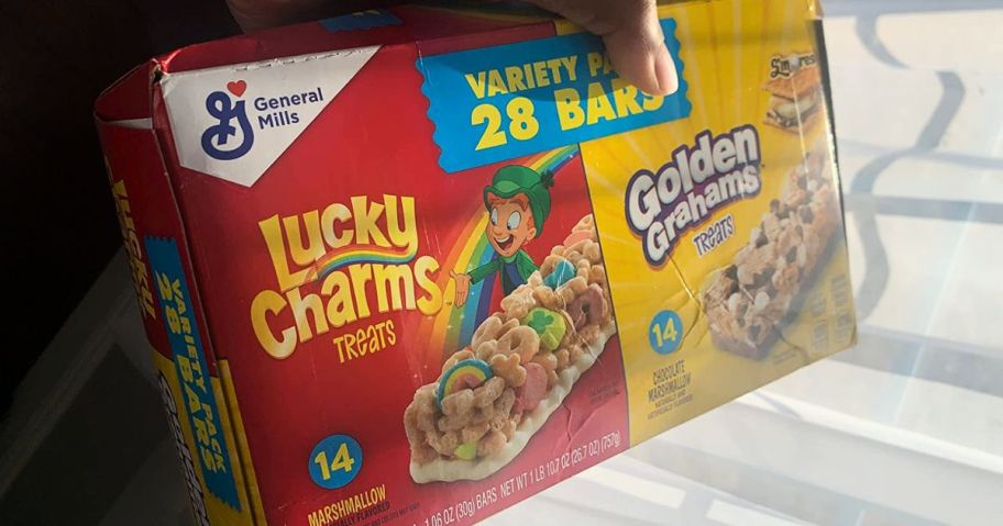 A person holding a box of Lucky Charms and Golden Grahams breakfast bars