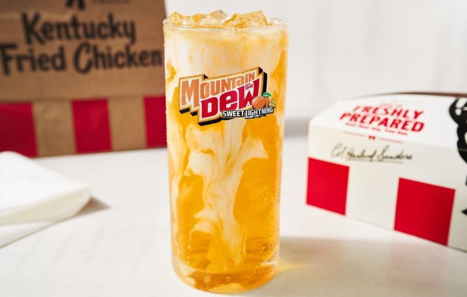 a glass of mountain dew peach soda next to a KFC food box