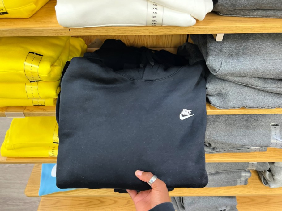 Women taking black Nike hoodie off of wooden store shelf