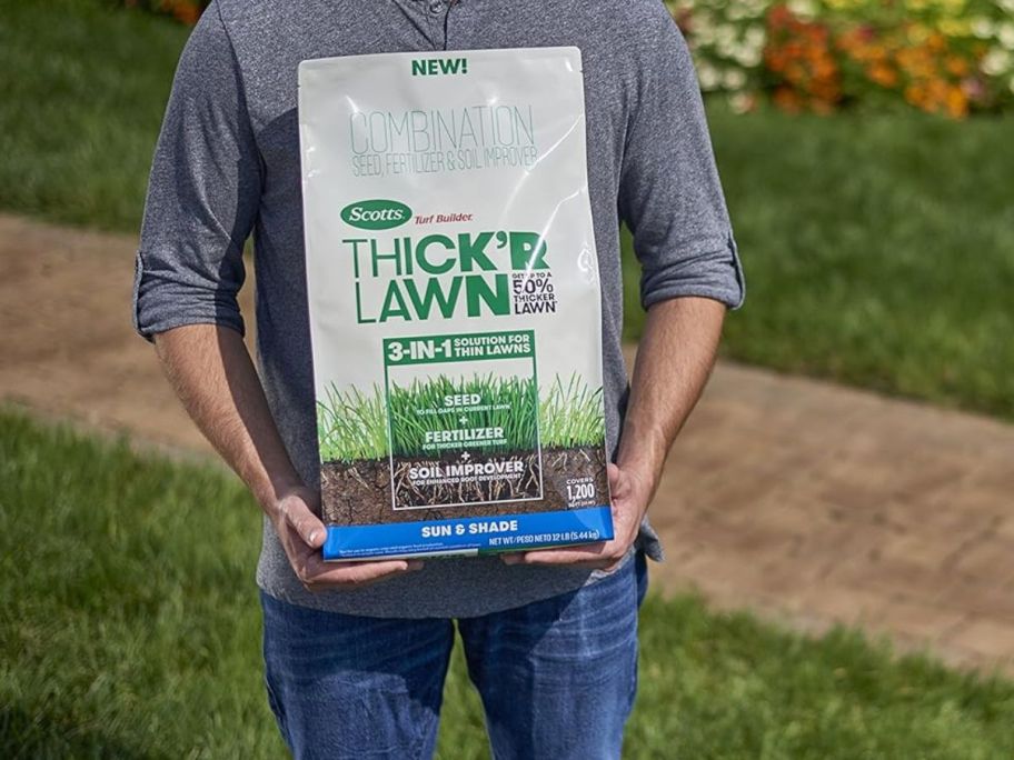 A man holding a large bag of Scotts Turf Builder THICK'R LAWN Grass Seed 