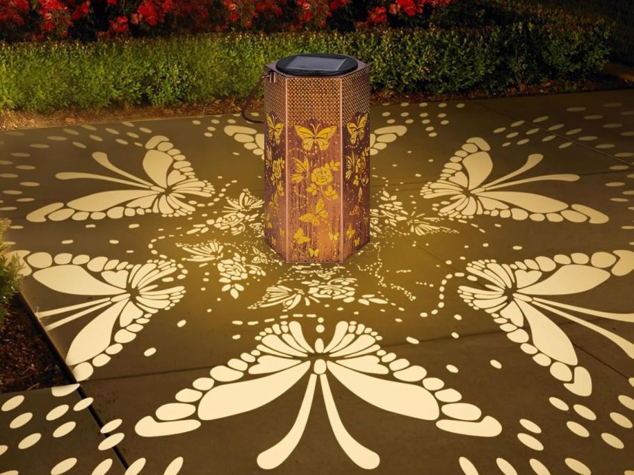 A butterrfly solar lantern with illuminated butterflies cast onto the ground around it