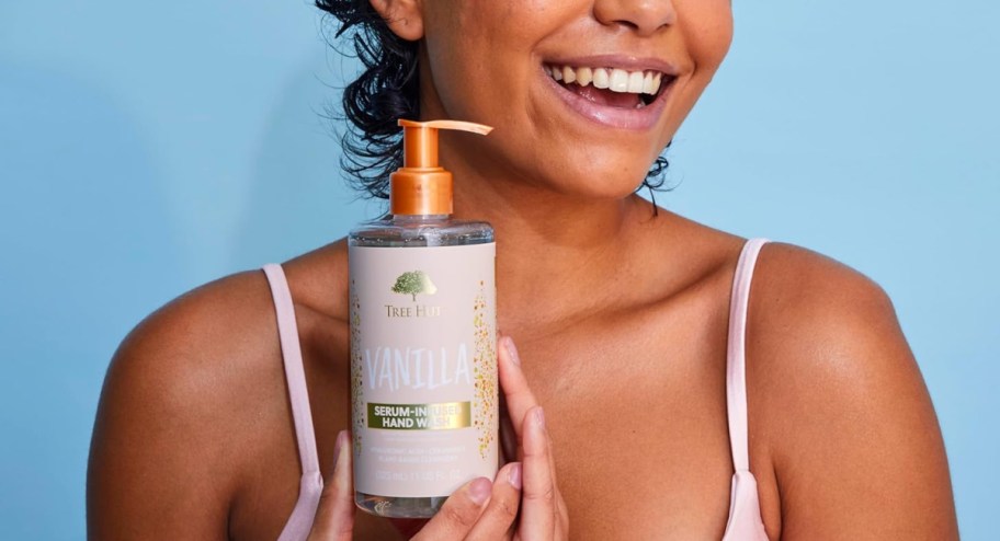 woman holding hand wash bottle in vanilla and smiling while wearing a tank top