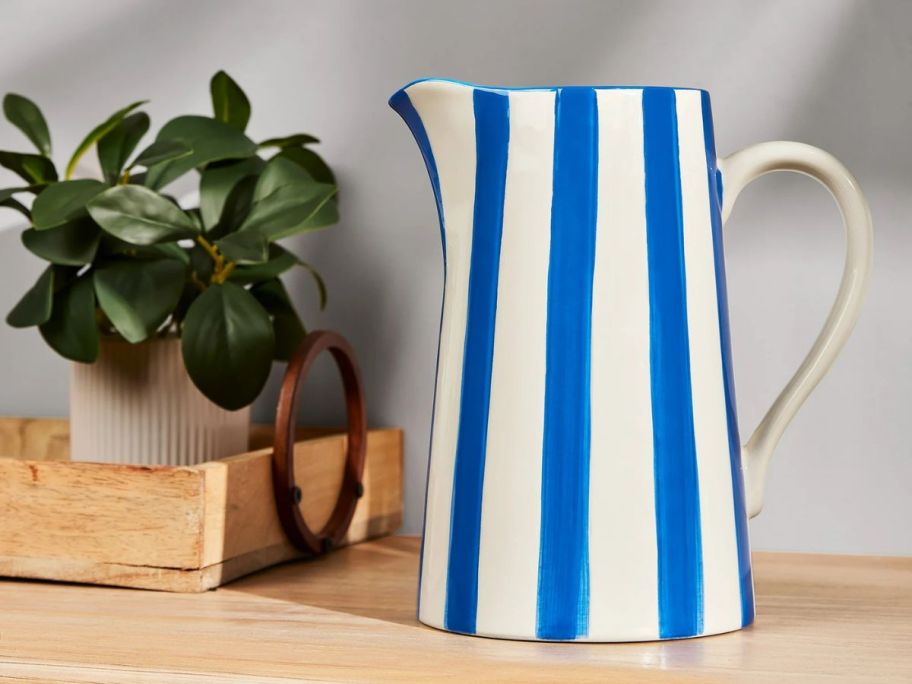 Mainstays by Becky G. & Alejandra Blue Stripe Ceramic Pitcher Vase next to a plant on a table