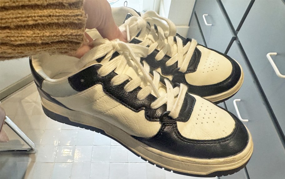 hand holding a pair of white and black sneakers