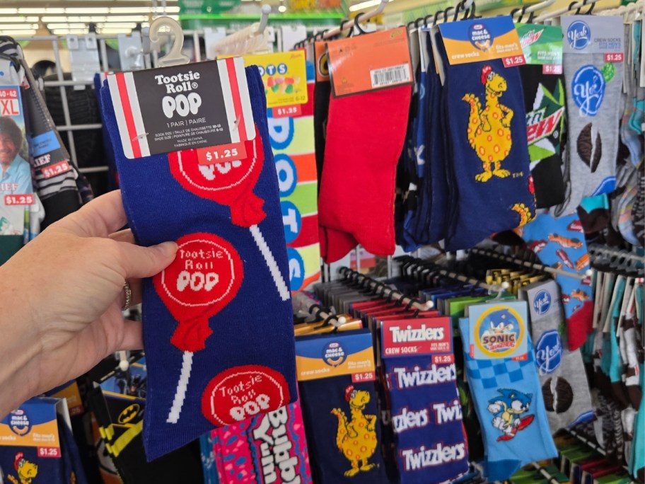 hand holding a pair of Blow Pop socks, more food-themed socks behind it on a store rack