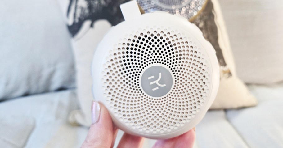person holding round white noise machine in their bedroom