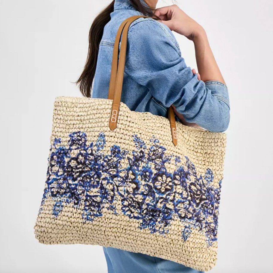 woman in blue shirt holding straw tote with blue flower design