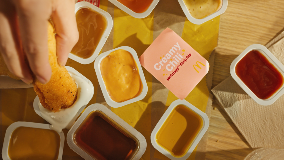 various cups of mcdonalds dipping sauces on a table, most open, one creamy chili one still sealed