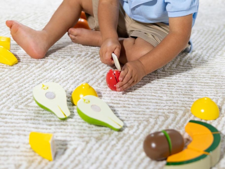 kid on floor pretending to cut a piece of fruit with the Melissa & Doug Cutting Fruit Set
