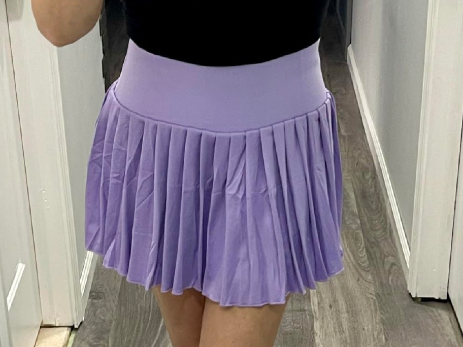 Woman wearing a black top and a purple skort in front of the mirror 