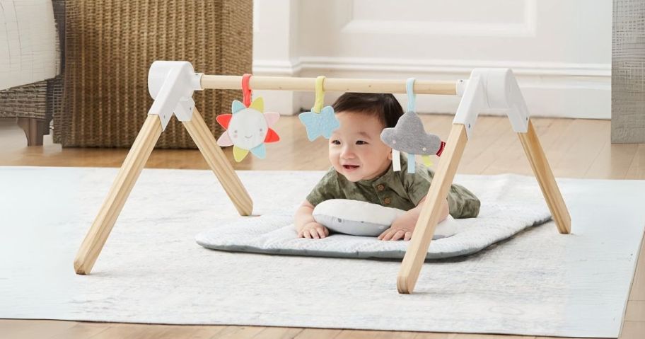 baby laying on tummy underneath Skip Hop Wooden Baby Gym on floor