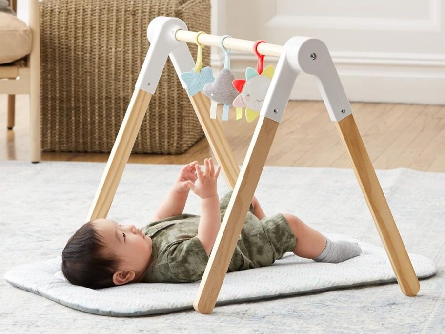 baby laying underneath Skip Hop Wooden Baby Gym on floor