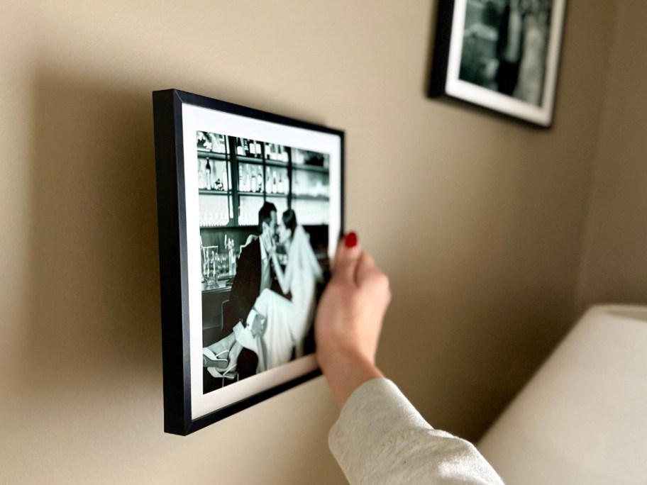 hand putting a black and white wedding photo in a black frame onto a wall