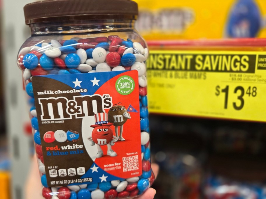hand holding a large container of red, white, and blue M&M's in a store aisle