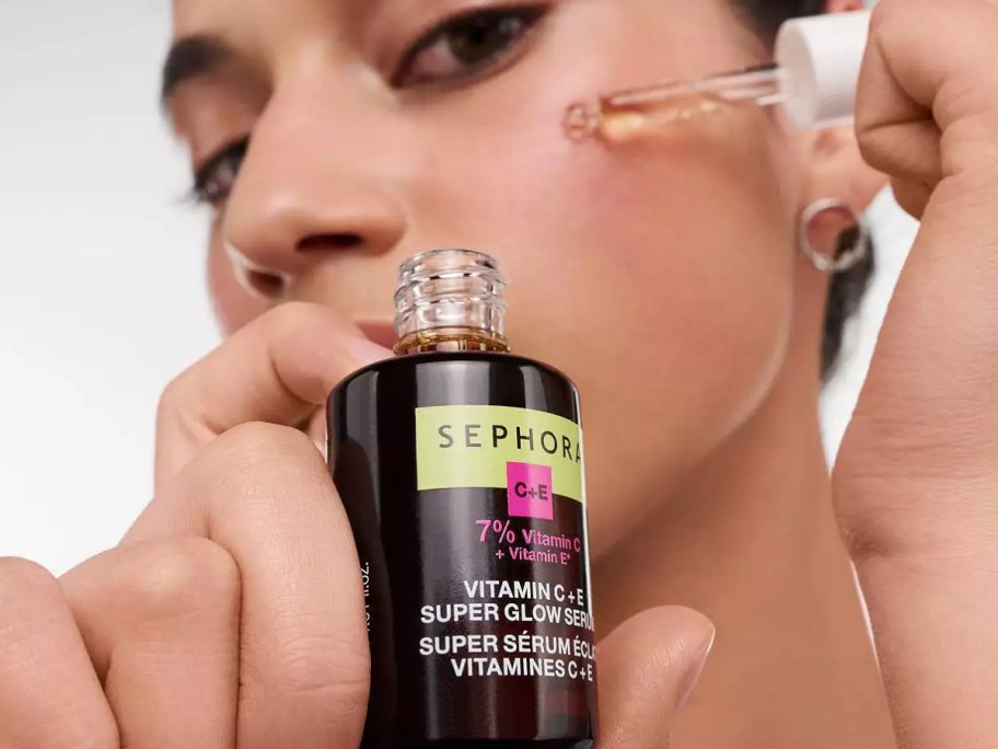 woman holding a bottle of facial serum in one hand and applying it with a dropper with the other hand