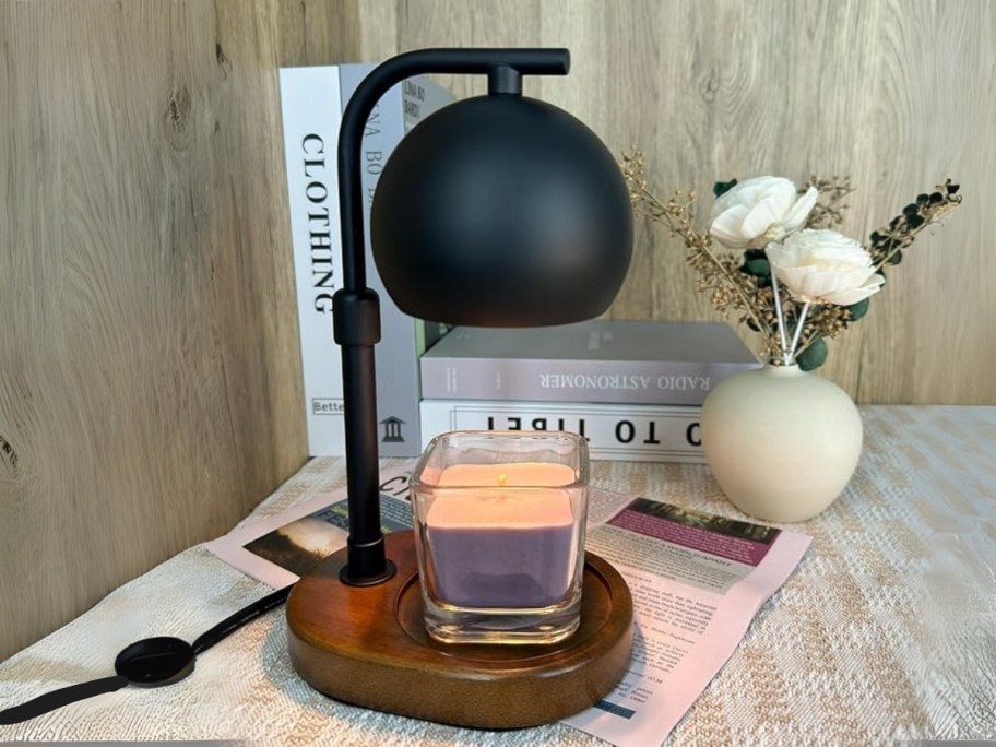 a black candle warmer lamp on a table with books and flowers behind it