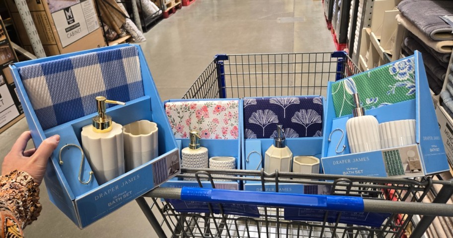 Sam's Club shopping cart with several bath accessory and shower curtain sets in it, person's hand holding 1 of them to the side