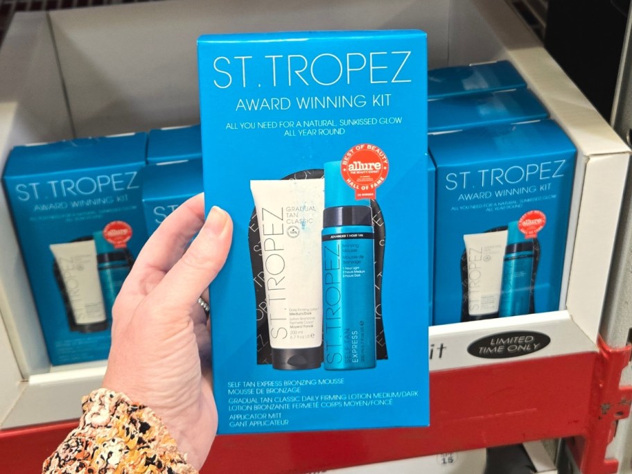 hand holding a box with a St. Tropez tanning kit, more on a store shelf behind it
