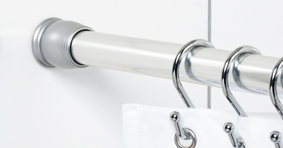 silver shower curtain rod with silver hooks holding a white shower curtain